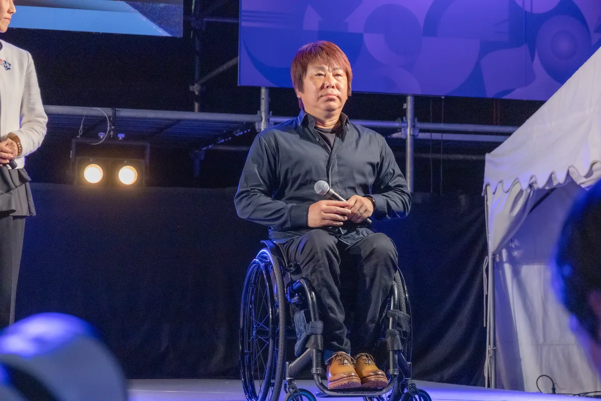 ONE HEART WORLDのステージでマイクを持って話す車いすバスケットボール元日本代表の根木慎志さん