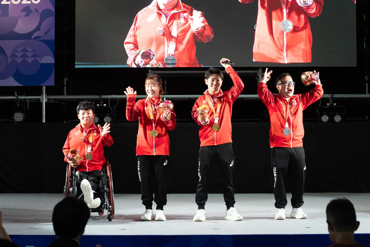 ステージで腕を上げる八木克勝選手と、北川雄一朗選手、山口美也選手、舟山真弘選手