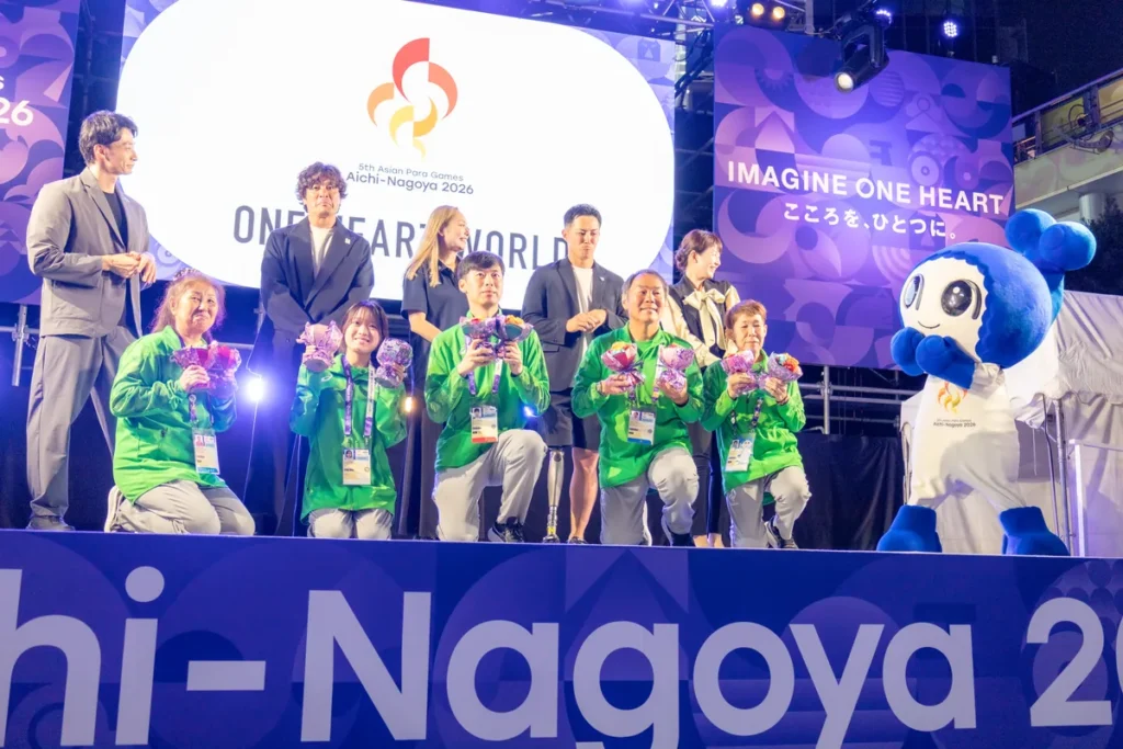 ONE HEART WORLD最後のセレブレーションで、花束を手にしたボランティアの皆さんとマスコットのウズミン、入江陵介さん、大畑大介さん、安藤美姫さん