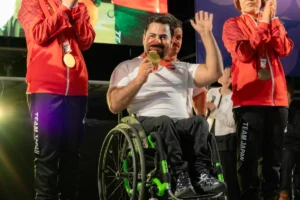 金メダルを掛け、車いすで手を振るムスタファ・ラディ選手。両脇に瀬戸勇次郎選手と藤原由衣選手