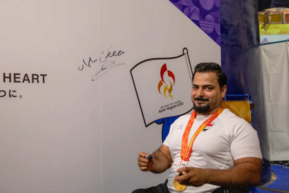 メディアセンターのサイン用の壁に大会ロゴの旗の絵に沿ってサインを書くムスタファ・ラディ選手
