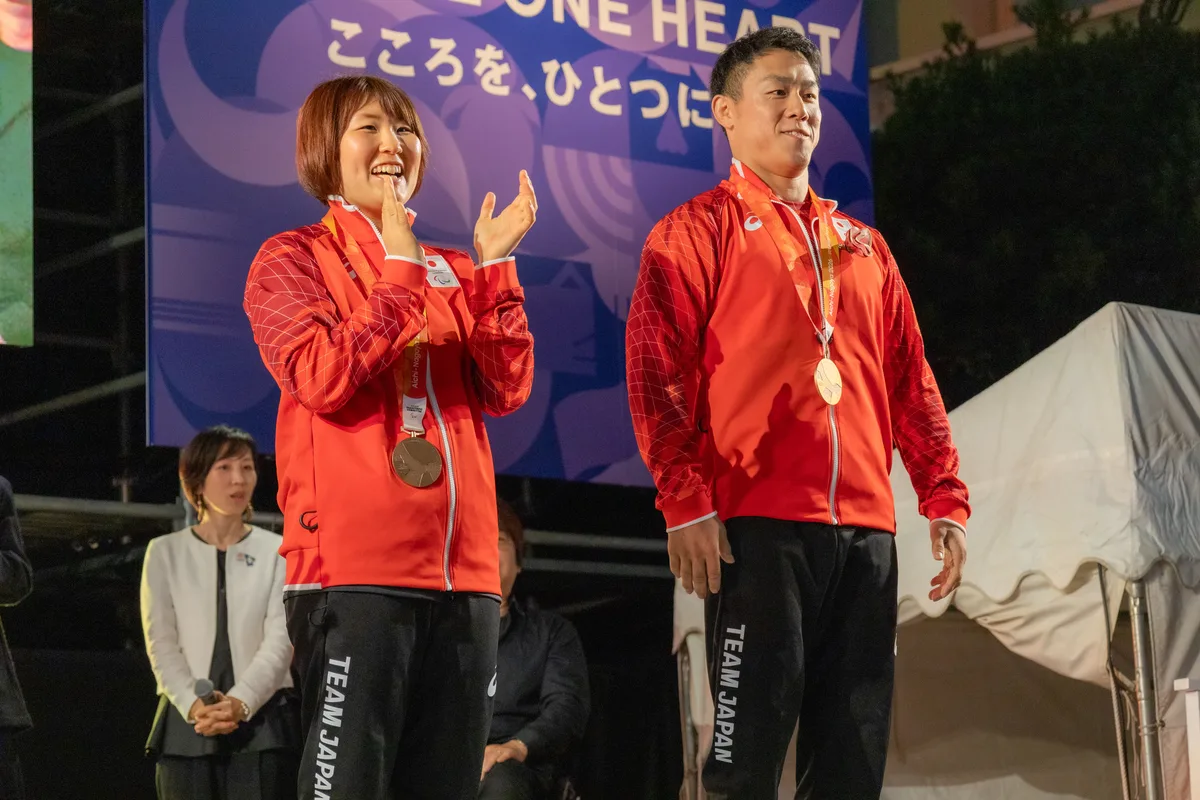 ONE HEART WORLDのステージで、銅メダルを掛けて会場の拍手に応える櫻井徹也選手と、拍手する藤原由衣選手