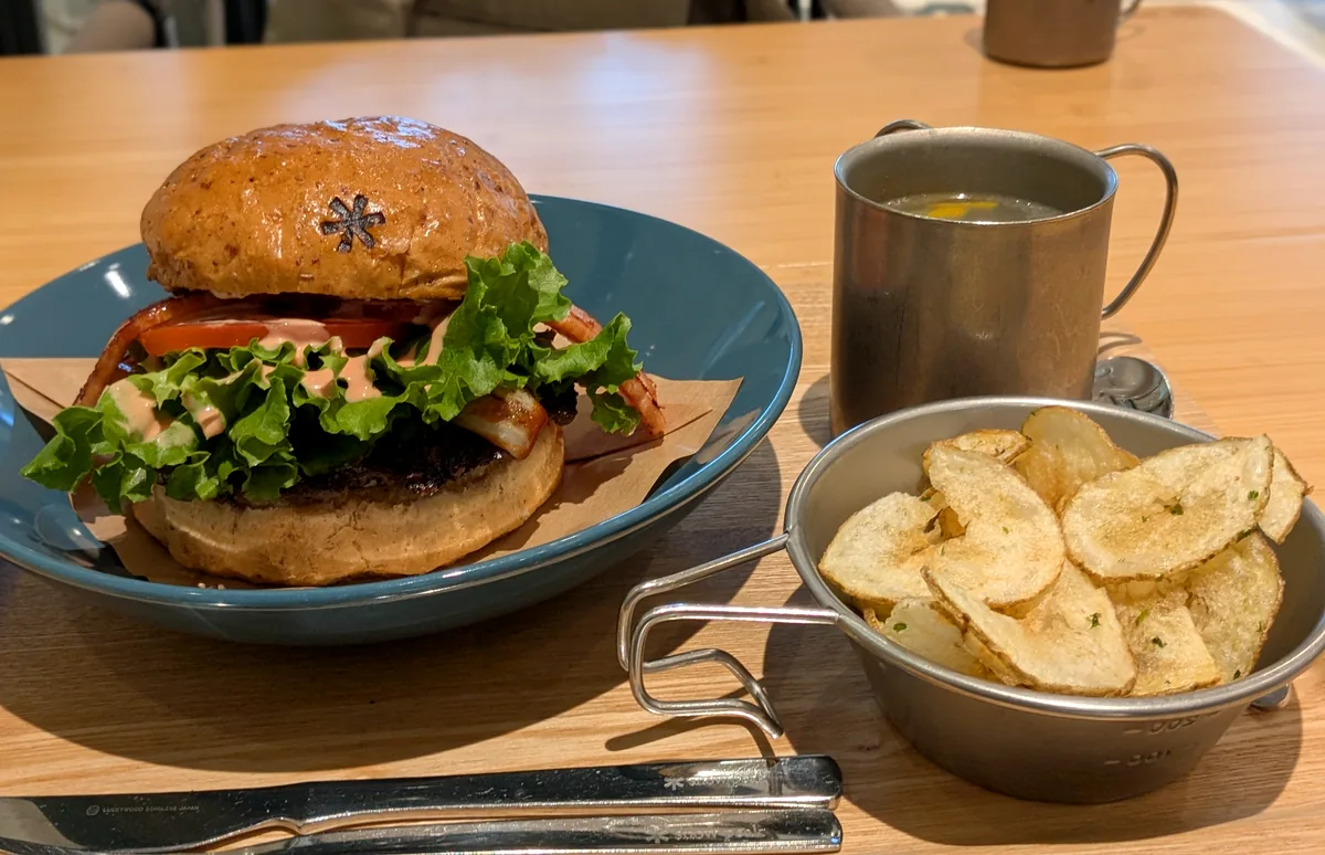 紺色のプレートにのったBLTバーガーと、ステンレスのボウルに入った手作りポテトチップス、マグのドリンク