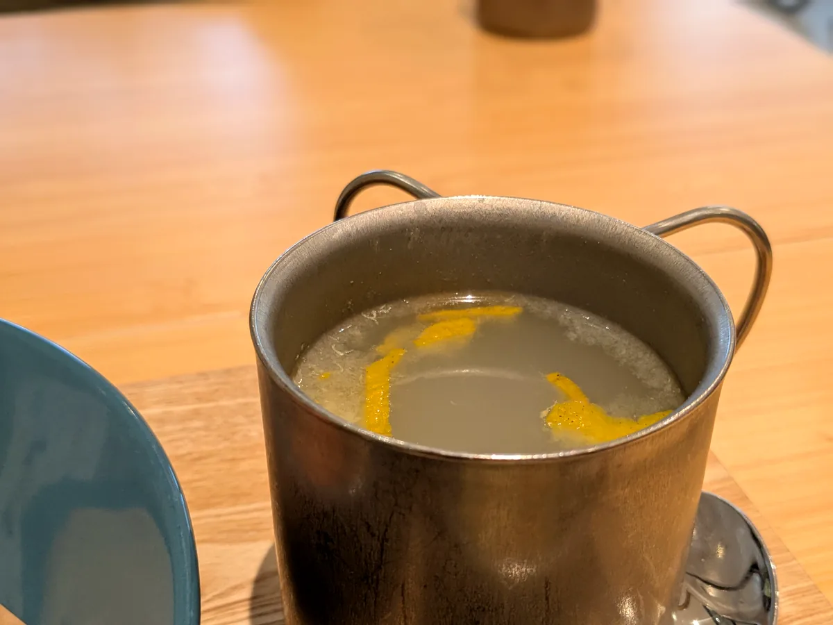 ステンレスのマグに入ったセットのホットドリンク。柑橘の皮が浮かんでいる