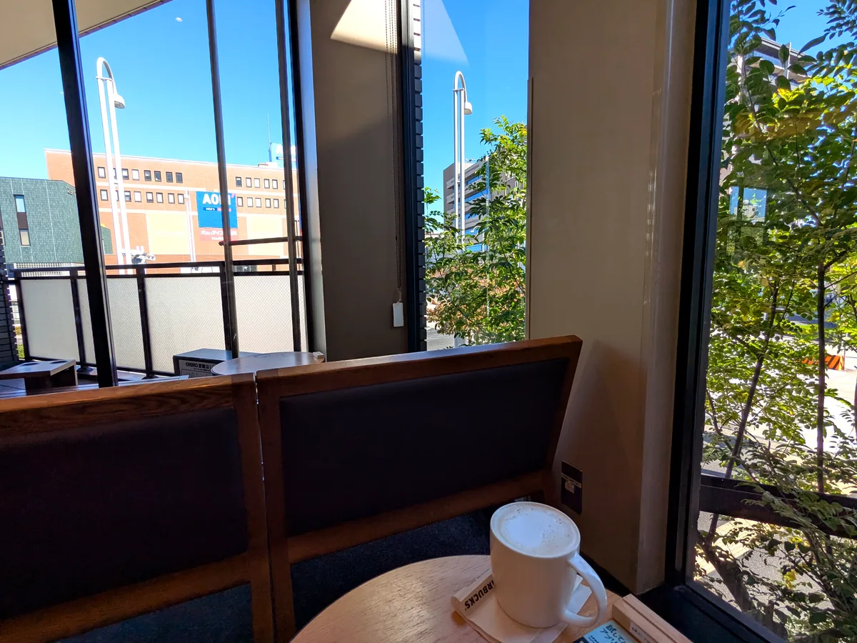 スターバックス御器所駅前店の2階窓側席。チャイ ティー ラテの向こうに阿由知通の街路樹と青空が広がる