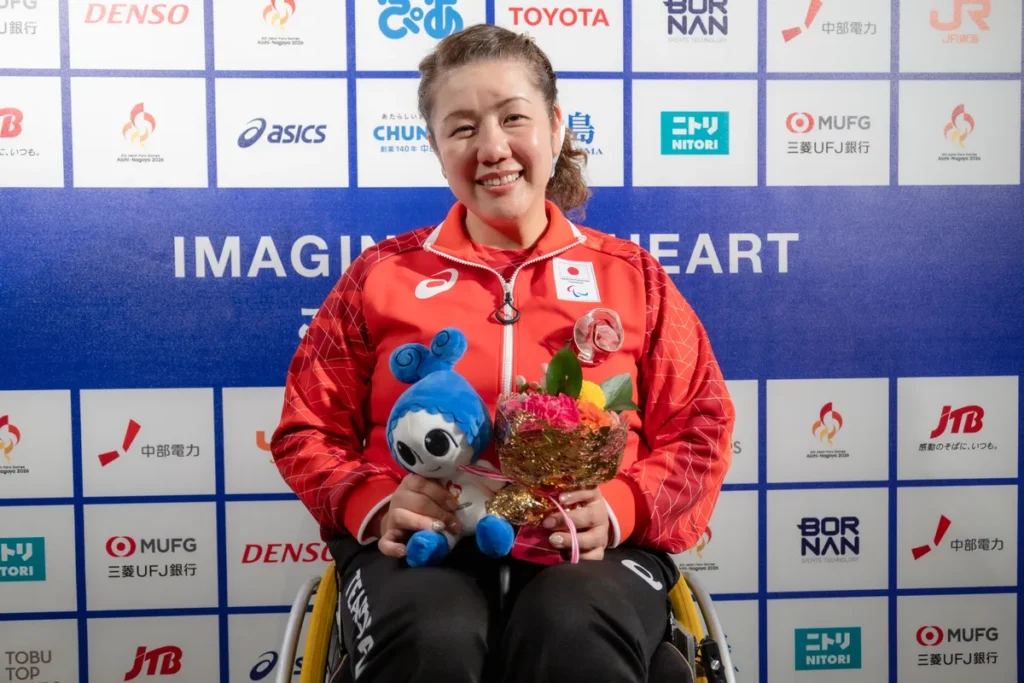 ミックスゾーンでウズミンのぬいぐるみと花束を手に笑顔を見せるパラ射撃の辻尾玲奈選手
