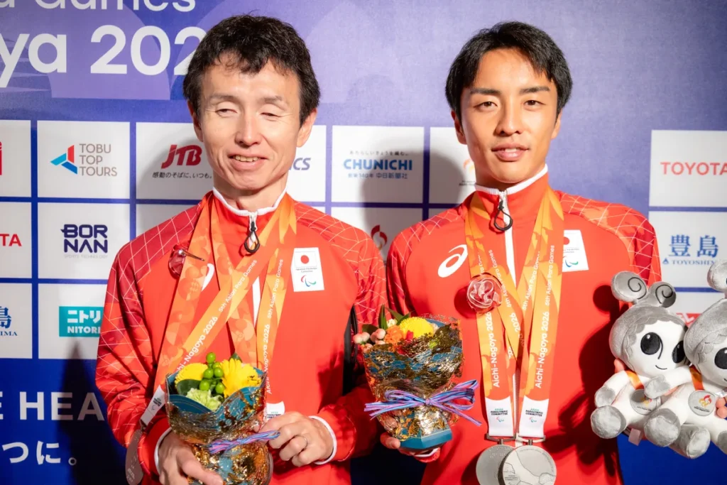 ミックスゾーンで銀メダルと花束を手に並ぶパラ陸上の和田伸也選手とガイドランナーの長谷部匠さん