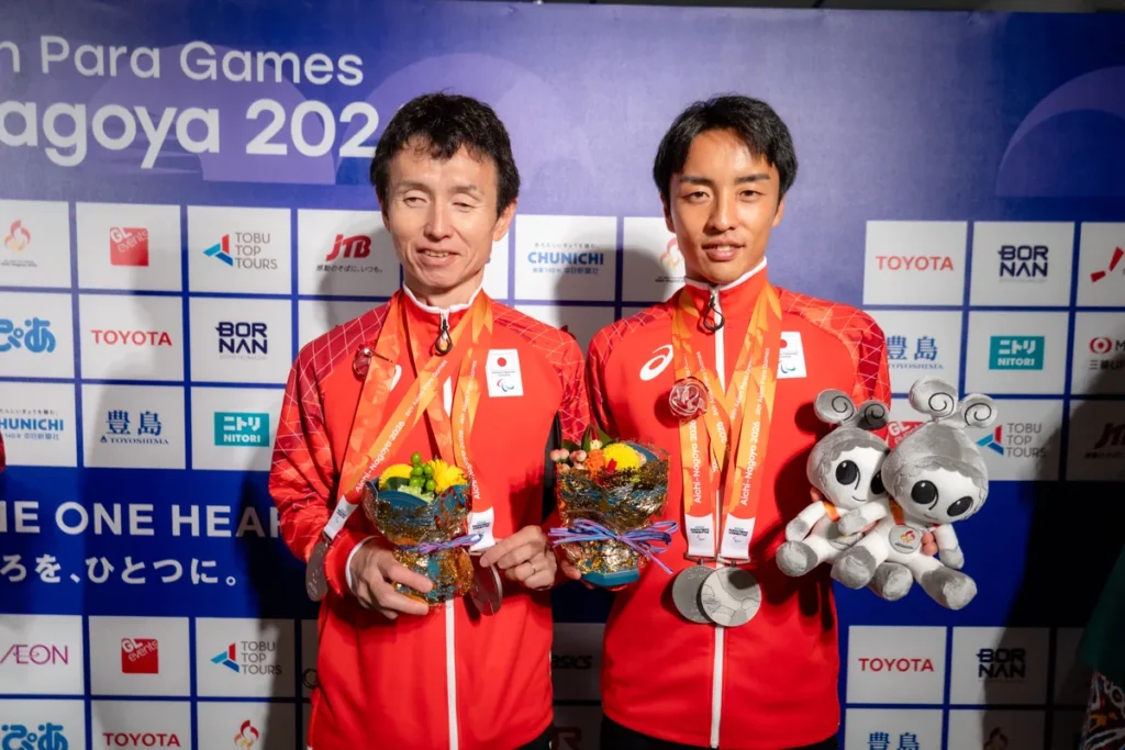 ウズミンのぬいぐるみと花束を手に並ぶ和田伸也選手と長谷部匠さん
