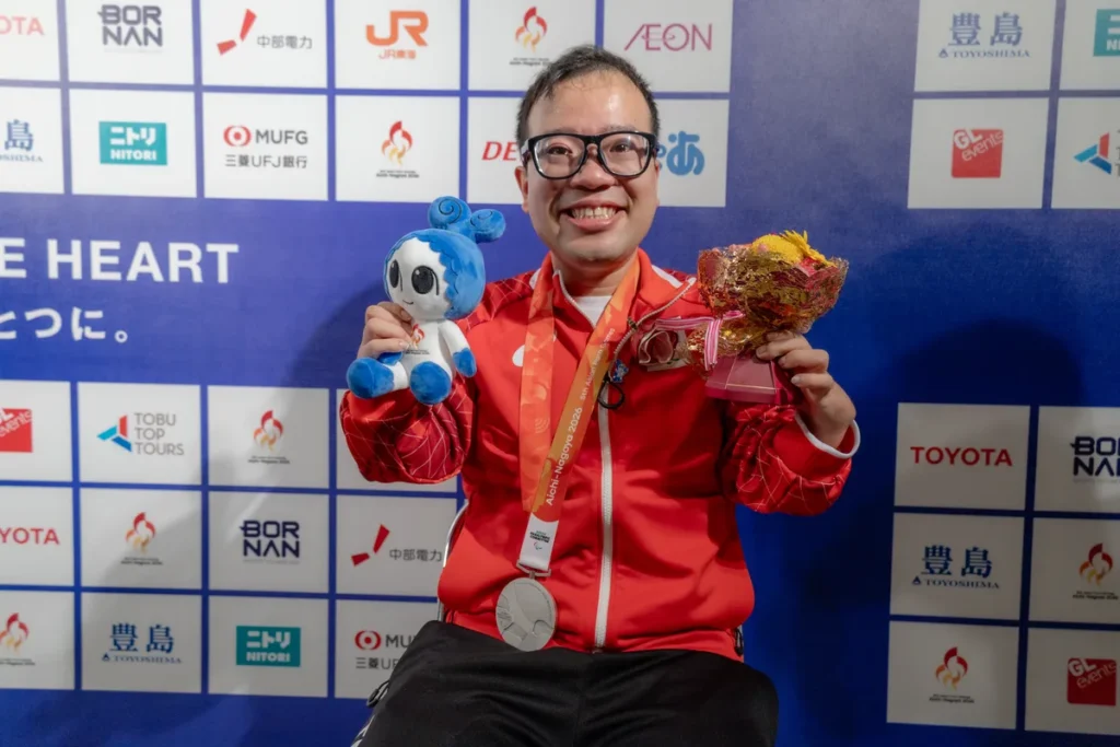 銀メダルとウズミンのぬいぐるみ、花束を手にする八木克勝選手
